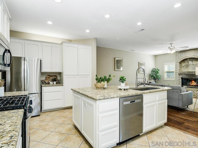 kitchen with appliances with stainless steel finishes, sink, white cabinets, light tile patterned floors, and light stone counters