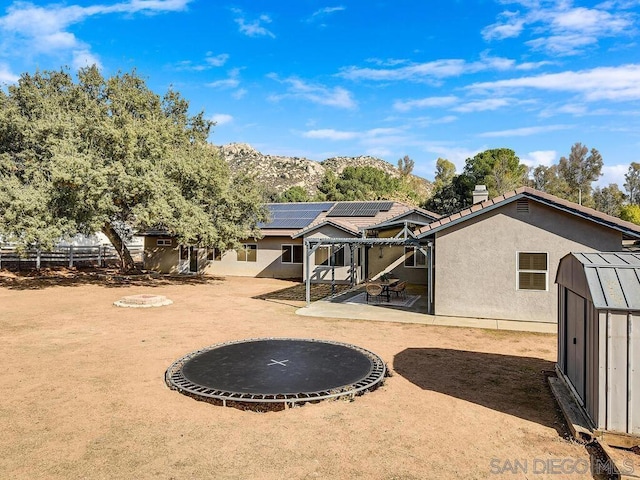 rear view of property featuring solar panels, a trampoline, a mountain view, a storage unit, and a patio