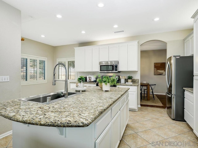 kitchen featuring sink, white cabinetry, light stone counters, an island with sink, and stainless steel appliances