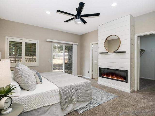 carpeted bedroom with ceiling fan, a spacious closet, access to outside, and a fireplace