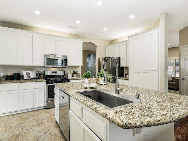 kitchen with stainless steel appliances, sink, a center island with sink, and light stone counters