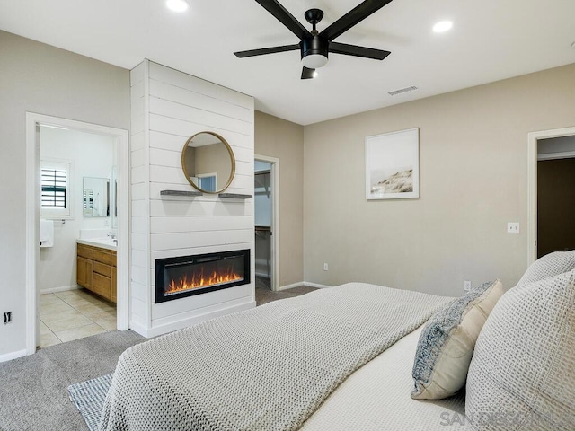 bedroom with ceiling fan, connected bathroom, a fireplace, a spacious closet, and light colored carpet