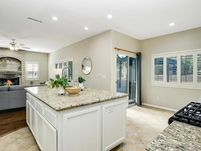 kitchen with white cabinetry, light stone counters, and a kitchen island with sink