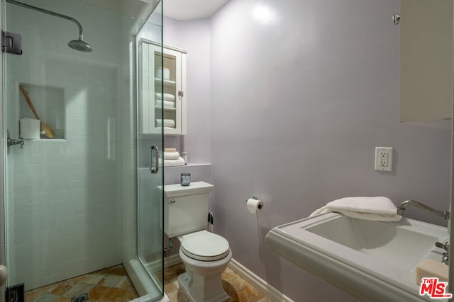 bathroom featuring sink, a shower with shower door, and toilet