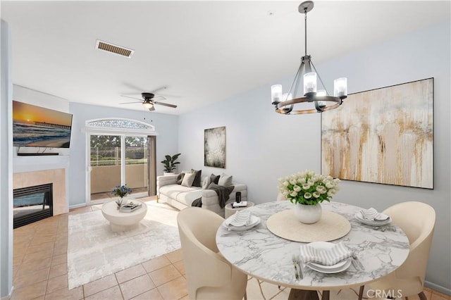 tiled dining room featuring ceiling fan with notable chandelier and a tile fireplace