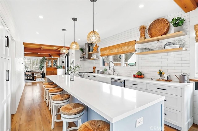 kitchen with light hardwood / wood-style flooring, white cabinetry, hanging light fixtures, a kitchen breakfast bar, and an island with sink