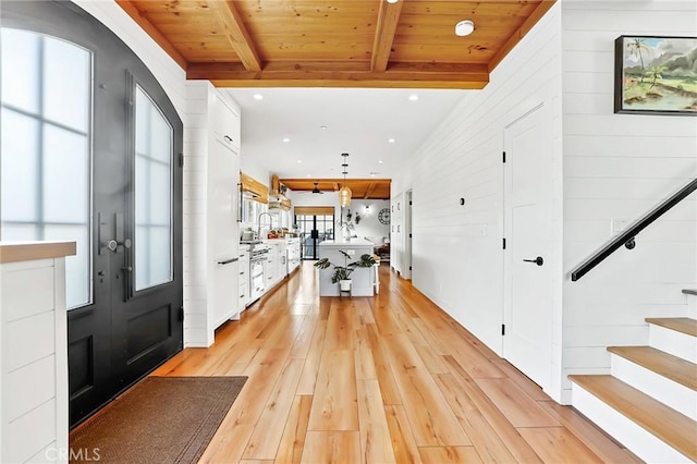 foyer with beamed ceiling, wood walls, wooden ceiling, and light wood-type flooring