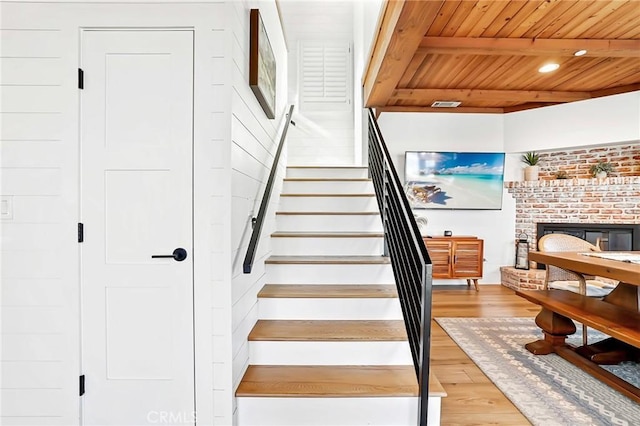 stairway featuring beam ceiling, wood ceiling, a fireplace, and hardwood / wood-style flooring