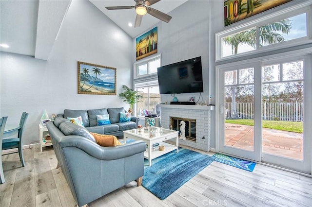 living room featuring a brick fireplace, a towering ceiling, light hardwood / wood-style flooring, and ceiling fan