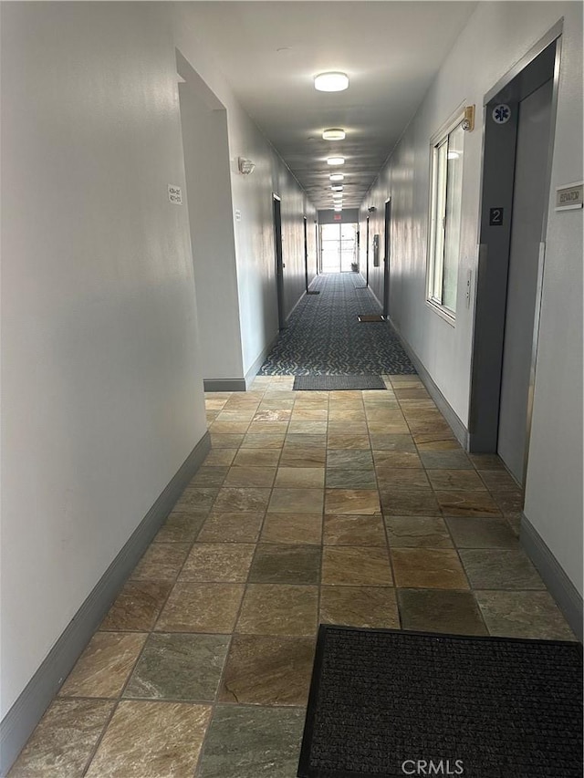 hallway featuring baseboards, elevator, and stone tile flooring