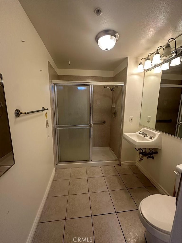 full bath with tile patterned floors, toilet, a stall shower, a sink, and baseboards