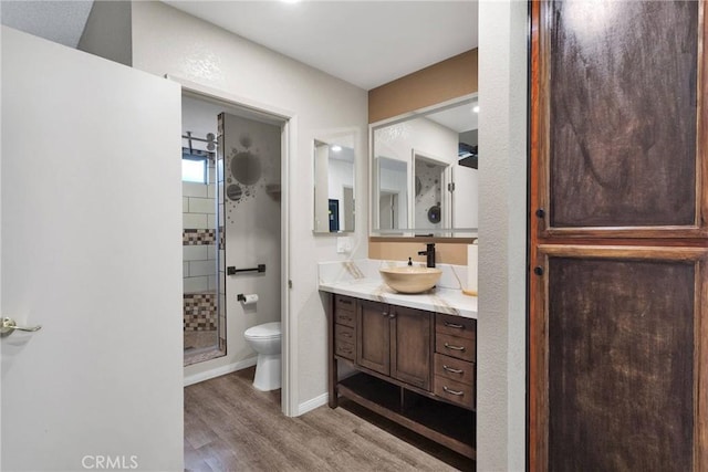 bathroom featuring wood-type flooring, a tile shower, vanity, and toilet