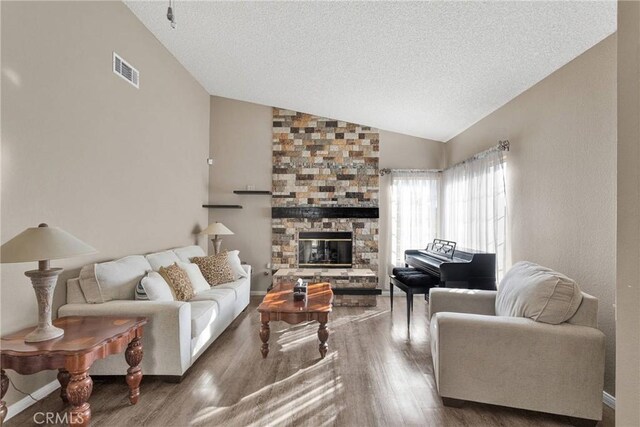 living room featuring hardwood / wood-style flooring, a stone fireplace, lofted ceiling, and a textured ceiling