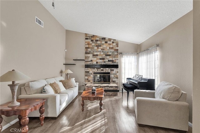 living room with lofted ceiling, a stone fireplace, wood-type flooring, and a textured ceiling