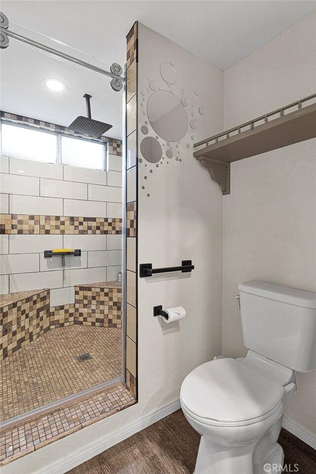 bathroom featuring wood-type flooring, toilet, and tiled shower