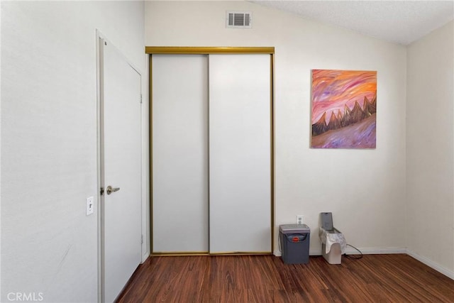 unfurnished bedroom with dark wood-type flooring, lofted ceiling, and a closet