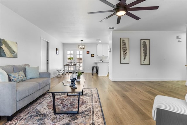 living room featuring ceiling fan with notable chandelier and light hardwood / wood-style floors