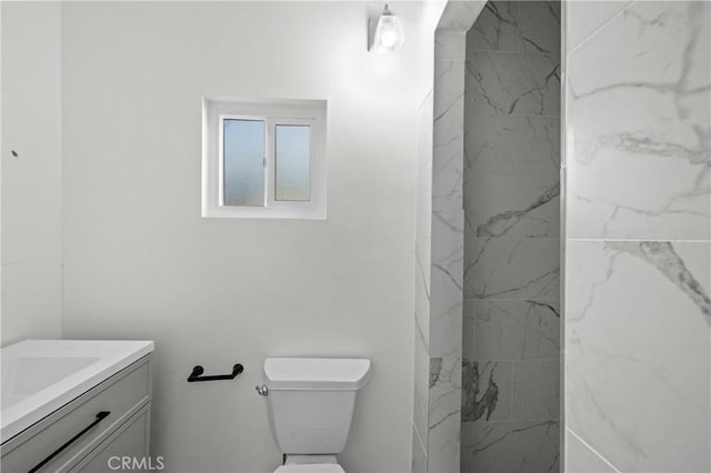 bathroom with tiled shower, vanity, and toilet