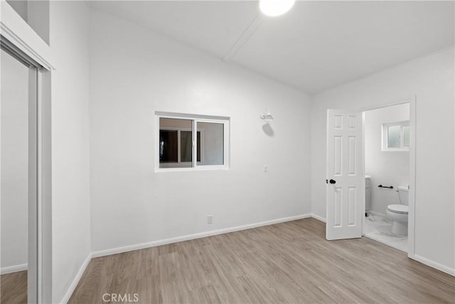 unfurnished bedroom featuring ensuite bathroom, vaulted ceiling, and light wood-type flooring