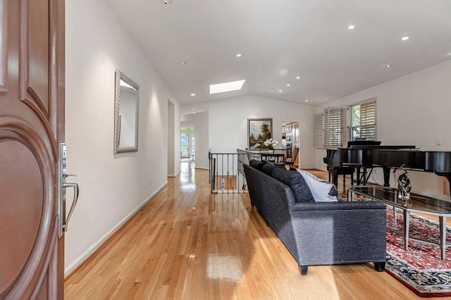 living room featuring a healthy amount of sunlight, vaulted ceiling with skylight, and light wood-type flooring