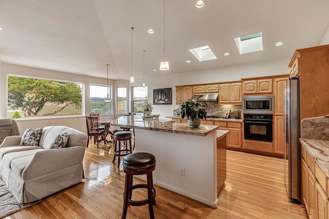 kitchen featuring a breakfast bar, appliances with stainless steel finishes, a kitchen island with sink, light stone counters, and decorative light fixtures