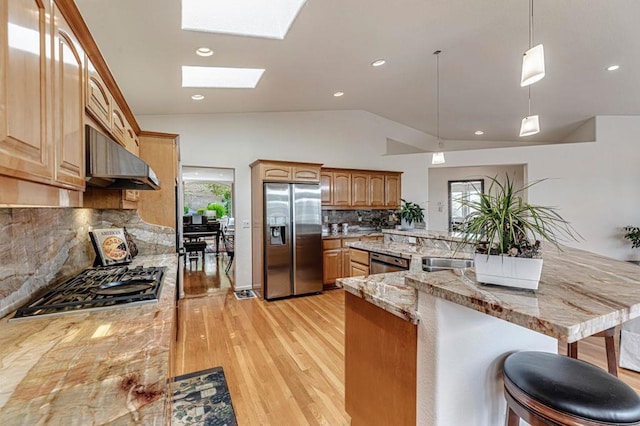 kitchen with appliances with stainless steel finishes, kitchen peninsula, a kitchen bar, and decorative light fixtures