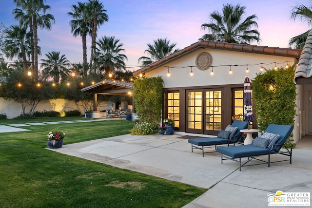 back house at dusk featuring a patio, a lawn, and french doors