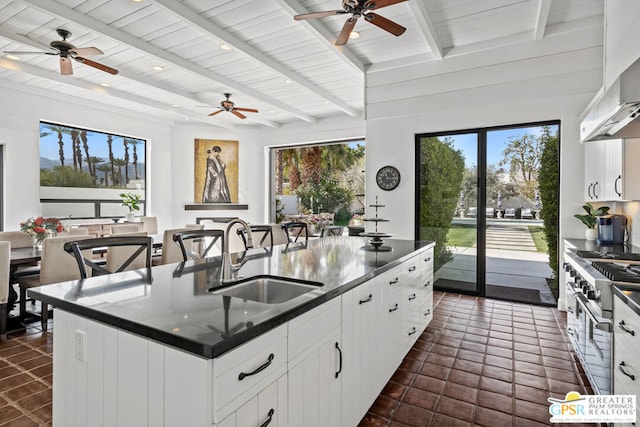 kitchen with sink, white cabinetry, stainless steel range, an island with sink, and wall chimney range hood