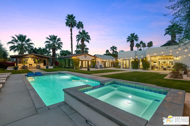 pool at dusk with an in ground hot tub, a gazebo, a patio area, and a lawn