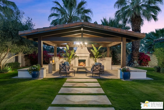 patio terrace at dusk with a gazebo, exterior fireplace, and a lawn