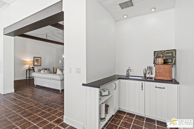 bar with white cabinetry, sink, and lofted ceiling with beams