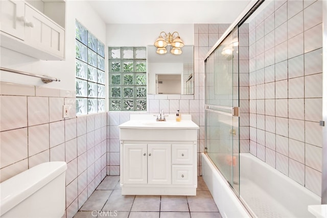 full bathroom with tile walls, bath / shower combo with glass door, vanity, tile patterned floors, and toilet