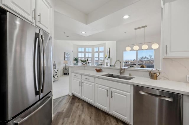 kitchen featuring appliances with stainless steel finishes, decorative light fixtures, sink, white cabinets, and light hardwood / wood-style flooring