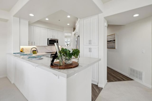 kitchen featuring a kitchen bar, sink, appliances with stainless steel finishes, kitchen peninsula, and white cabinets