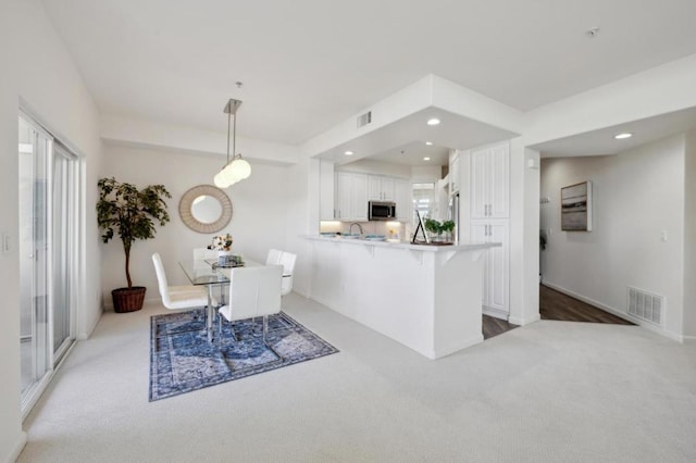 kitchen with sink, light carpet, kitchen peninsula, pendant lighting, and white cabinets