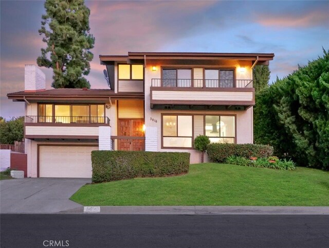 view of front of property featuring a garage, a balcony, and a lawn