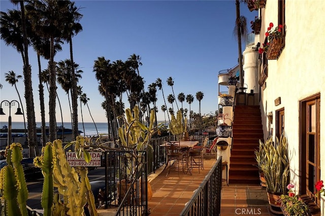 balcony featuring outdoor dining space, stairway, and a water view