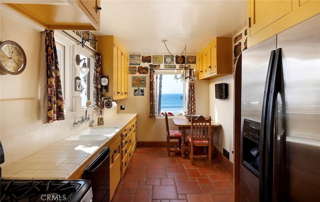 kitchen featuring a sink, baseboards, black dishwasher, tile counters, and stainless steel fridge with ice dispenser