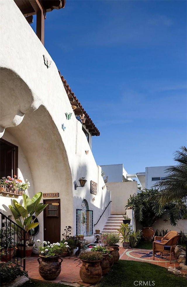 view of front of home featuring a tile roof, stucco siding, a patio, and stairs