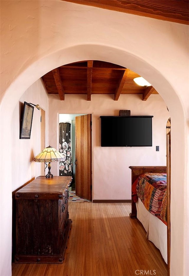 corridor featuring baseboards, beam ceiling, arched walkways, and wood finished floors