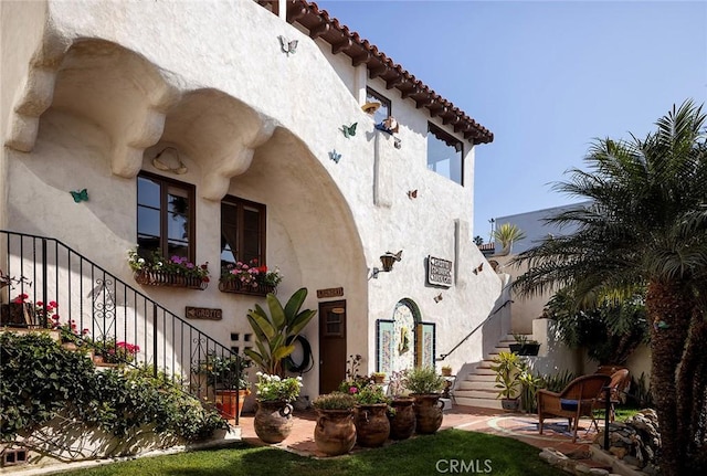 exterior space with stairs, a tile roof, and stucco siding