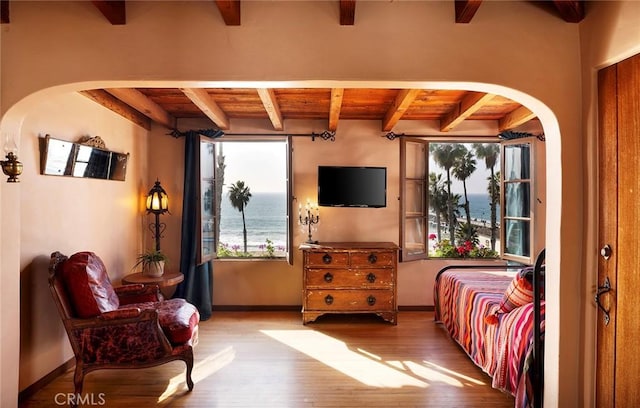 bedroom featuring arched walkways, light wood finished floors, beam ceiling, and baseboards