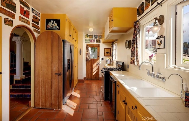 kitchen featuring appliances with stainless steel finishes, a sink, tile counters, and a healthy amount of sunlight