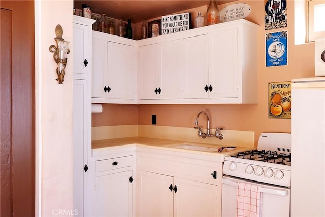 kitchen featuring white range with gas cooktop, sink, and white cabinets