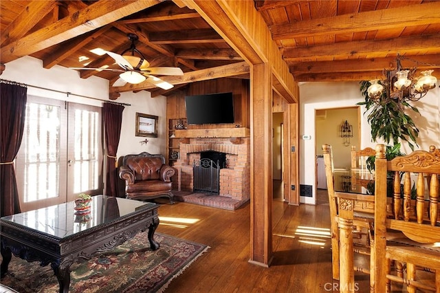 living room with dark wood-type flooring, vaulted ceiling with beams, wood ceiling, a fireplace, and ceiling fan with notable chandelier