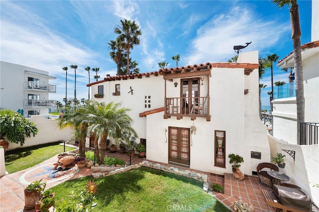 view of front of property featuring a balcony, fence, french doors, stucco siding, and a patio area