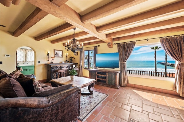 living room with an inviting chandelier, stone tile flooring, beam ceiling, and baseboards