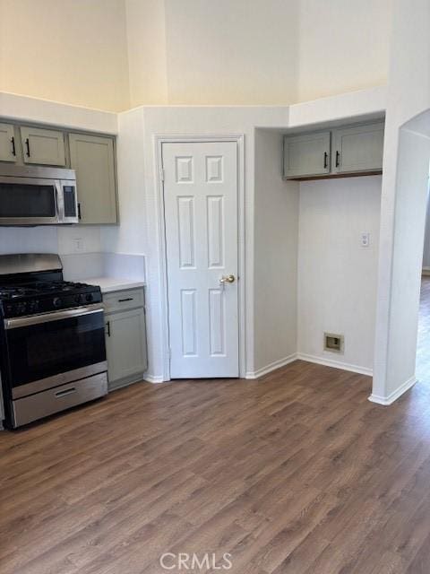 kitchen with gray cabinets, a towering ceiling, stainless steel appliances, and dark hardwood / wood-style flooring