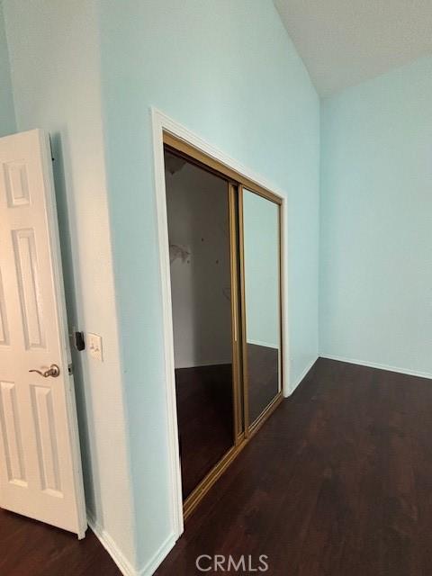 unfurnished bedroom featuring vaulted ceiling, dark hardwood / wood-style floors, and a closet