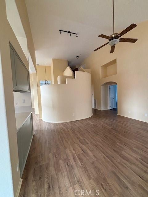 unfurnished living room with dark wood-type flooring, high vaulted ceiling, ceiling fan, and track lighting